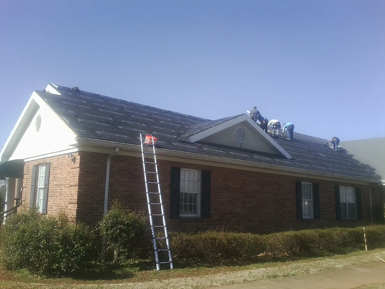 Crew tearing shingles off a brick ranch roof with a ladder set — Metal Roof Repair work by our crew in Saint David