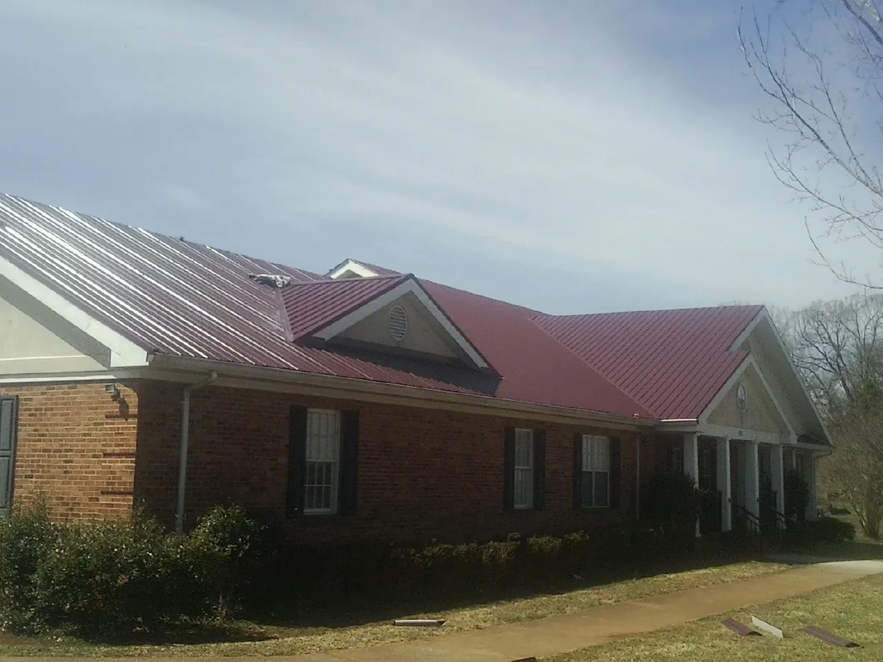Red metal roof with gabled entries on a long brick building, from a Hail Damage Roof Repair job in Saint David