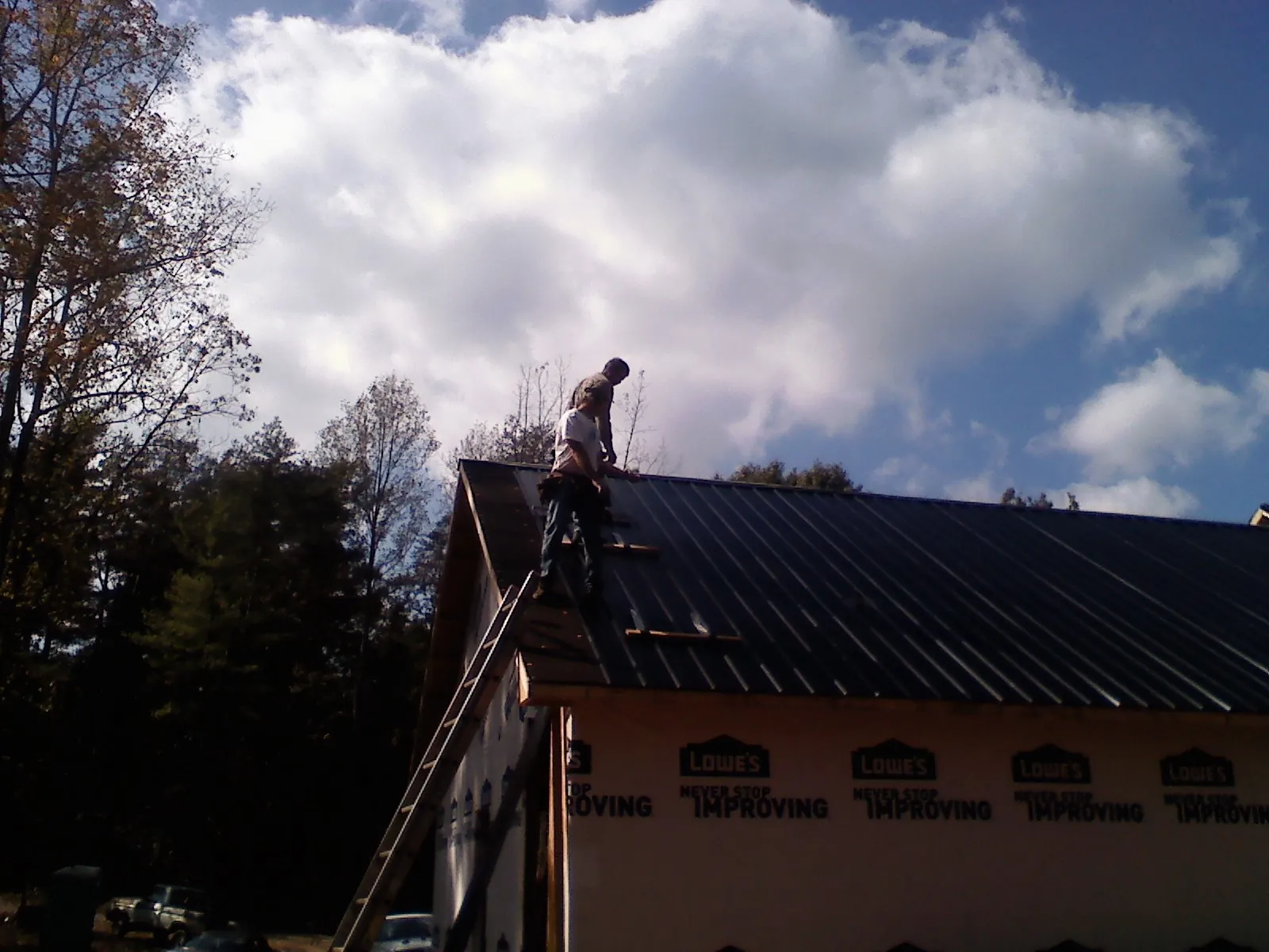 Roofer fastening dark metal panels high against a cloudy sky, from a Roof Inspection job in Saint David