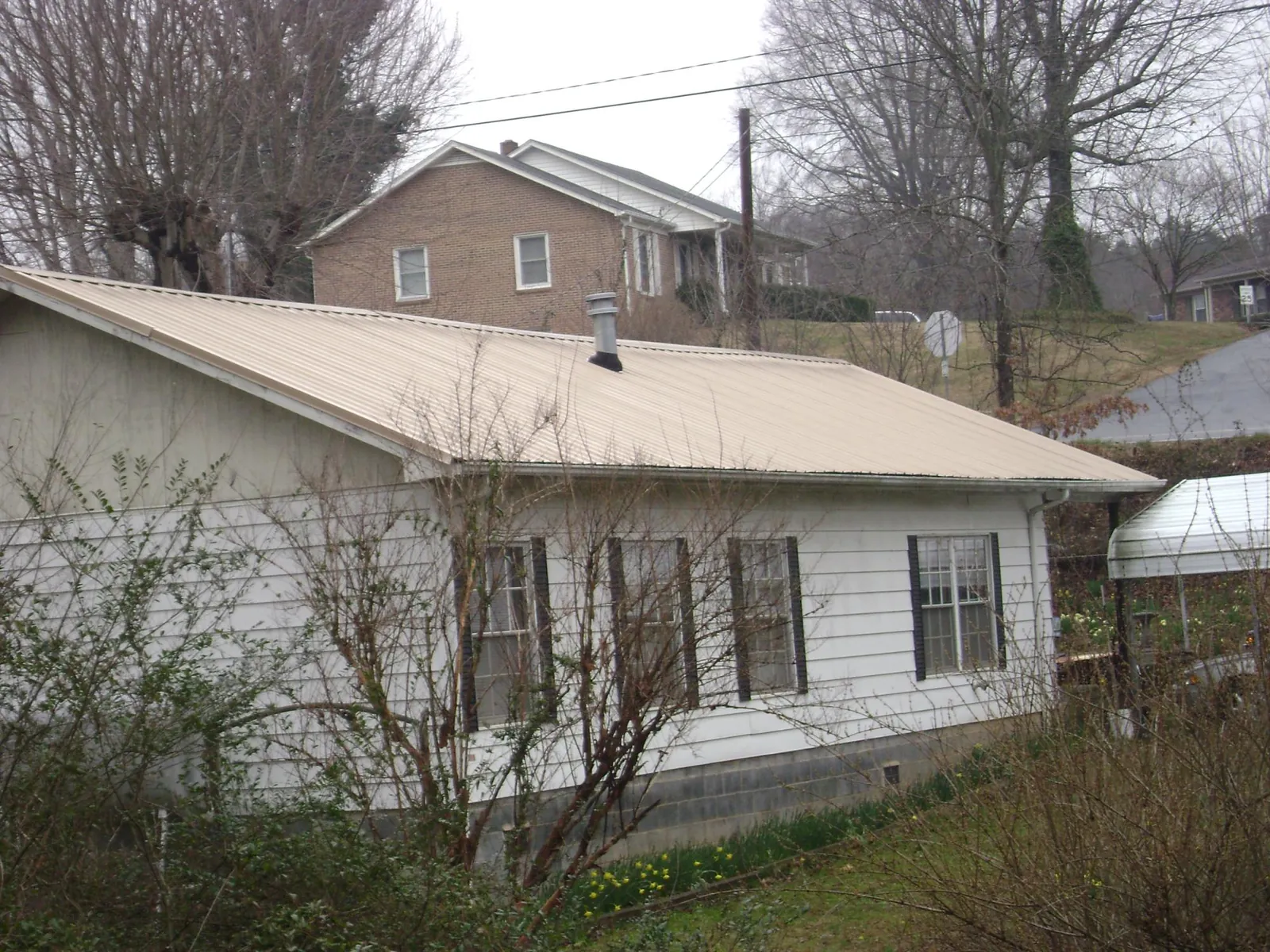 Tan metal roof on a white sided house set into a hillside — Commercial Roofing by Roofing Brothers in Saint David